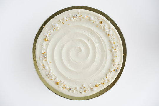 Cake with white cream, decorated with silver and gold confectionery sprinkles and gold leaf on a white background. Picture for a menu or a confectionery catalog. Top view.