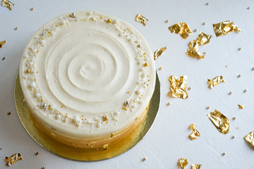 Cake with white cream, decorated with silver and gold confectionery sprinkles and gold leaf on a white background. Picture for a menu or a confectionery catalog. Top view.
