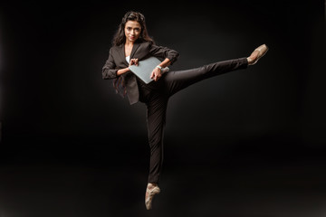 businesswoman in suit and ballet shoes with laptop on black background