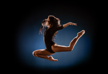 side view of beautiful ballerina in black bodysuit jumping on dark background © LIGHTFIELD STUDIOS