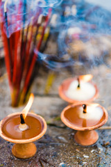 Terra-cota oil lamps as religious offerings at temple in Nepal. Incence sticks over blurred background.