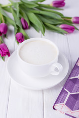 White cup with coffee cappuccino, book and purple tulips on a white background. Free space