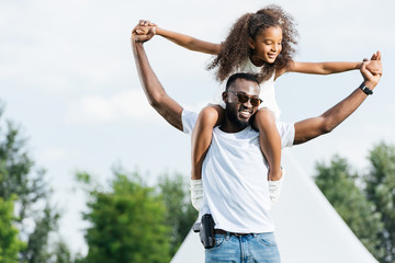 african american policeman with gun holding daughter on shoulders in amusement park