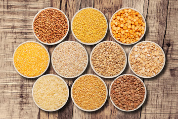 Grain and cereal food selection in porcelain bowls on wooden table, top view