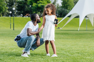 african american daughter holding father police badge in park