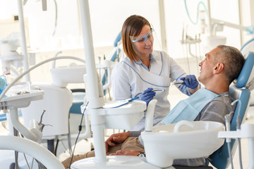 Dentist  in dental office talking with male patient and preparing for treatment.
