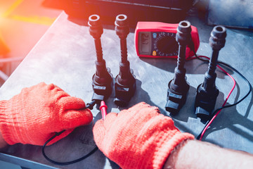 Mechanic man with digital multimeter testing ignition coil