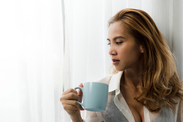 Happy Asian woman drinking coffee and looking out window, lifestyle concept.