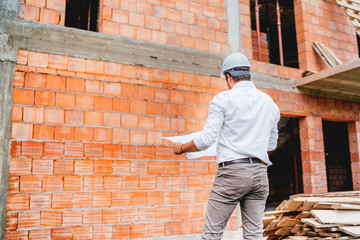 construction engineer reading plans, working on building construction site. brick walls, infrastructure on construction site