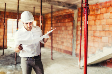 Construction industry engineer working on house building site - reading paper plans and coordinating workers