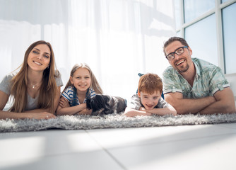 Fototapeta premium Happy family lying on carpet in room at new home