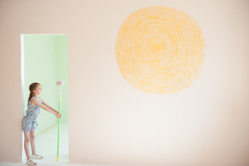 beautiful girl with paint roller in doorway of new room with sun painted on wall