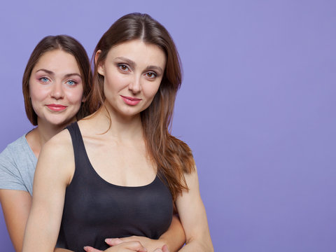 Two attractive young women standing huging, one besides another one. One with blue eyes, another one with dark brown, the both are brunettes. Isolated, studio, models, copy space. Diversity people
