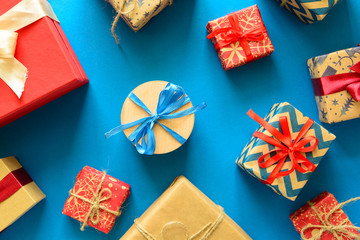 Top view on Christmas gifts wrapped in gift paper decorated with ribbon on blue paper background....