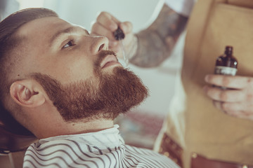 The barber applies the beard oil with a dropper. Photo in vintage style