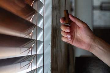 The man's right hand holds one of the control strings of the wooden shutters on the window.