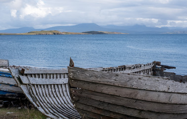 Fototapeta na wymiar Ruins of small boat on the beach at Polbain, north of Ullapool. In background, view of the Summer Isles taken from the Scottish mainland on the west coast of Scotland. 