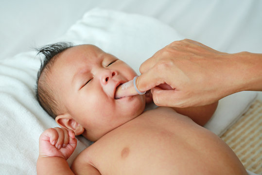 Close-up mother hand clean infant tongue and gum with soft rubber brush. Baby healthcare.