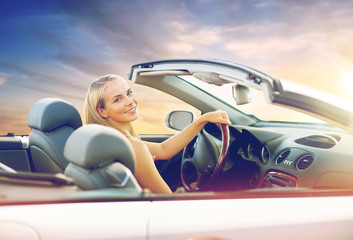 travel, road trip and people concept - happy young woman driving convertible car over sunset sky background