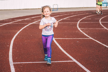 Fototapeta premium Little girl running on the track in stadium. Running track in stadium.