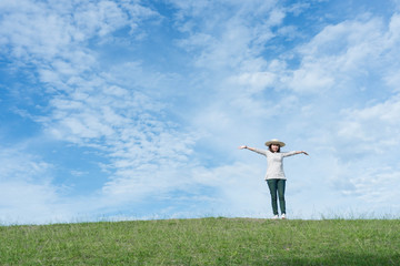 Standing woman raised her hands on the mountain, natural green and beautiful sky.
