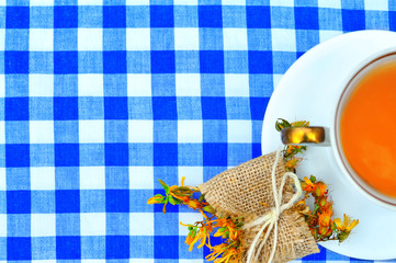 Rustic white porcelain cup with hot tea a herb wrapped up as a gift on a  blue-white checkered...