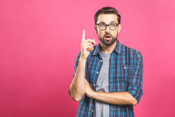 Portrait of an excited happy man pointing finger up at copyspace isolated on a pink background....