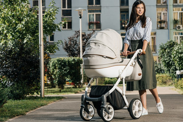 attractive mother walking with baby stroller on street and looking away