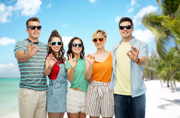friendship, travel, tourism and summer holidays concept - group of happy smiling friends in sunglasses showing ok hand sign over tropical beach background in french polynesia