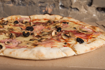 Pizza with ham, black olives, ham, spices. Italian pizza. Home made food. Concept for a tasty and hearty meal, lunch. Brown wooden background. Food background, pizza texture. Close up of pizza.