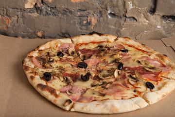 Pizza with ham, black olives, ham, spices. Italian pizza. Home made food. Concept for a tasty and hearty meal, lunch. Brown wooden background. Food background, pizza texture. Close up of pizza.