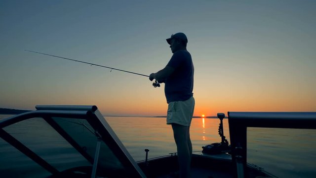 Male angler is casting a fishing rod into a sunlit lake 