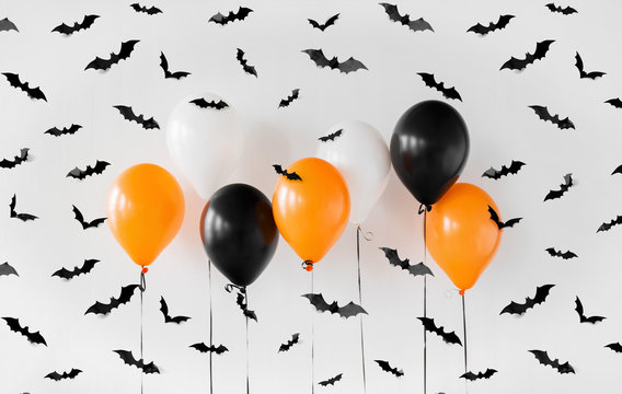 holidays, decoration and party concept - orange, black and white air balloons for halloween with black flying bats on white background
