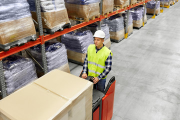 logistic business, shipment and loading concept - loader in helmet operating forklift at warehouse