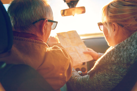 Elderly Loving Couple Traveling In Car On Vacation. They Are Looking On A Map For Direction.