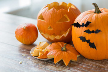 halloween, holidays and decoration concept - jack-o-lantern or carved pumpkins with bats on wooden table at home