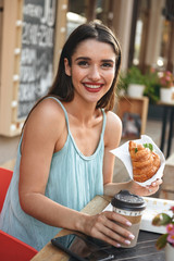 Woman sitting in cafe outdoors while eating croissant.