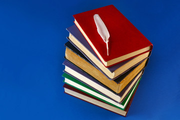 a stack of old books and a feather on a blue background