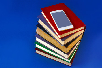 a stack of old books and a white smartphone on a blue background
