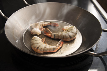 fresh king prawns half roasted in hot oil  in an iron pan on a black stove, food and cokking concept, selected focus, narrow depth of field