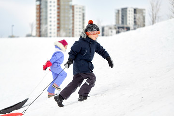 Fototapeta na wymiar childhood, sledging and season concept - happy little kids with sleds climbing snow hill in winter