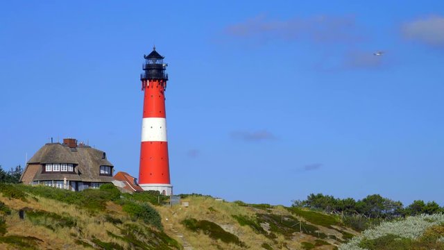 Leuchtturm H&ouml;rnum Sylt mit D&uuml;nen Landschaft  Reetdach H&auml;usern und  blauen Himmel

