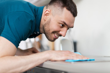 household and people concept - man wiping table with cloth cleaning cooker at home kitchen
