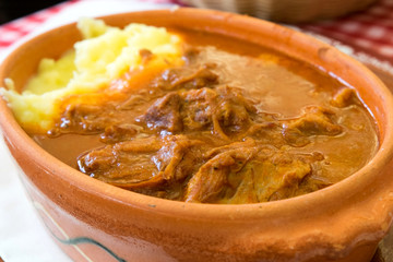 Delicious dish from Serbian and Hungarian cuisine - meat goulash (gulas) served with mashed potatoes in a ceramic pot