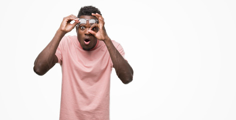 Young african american man wearing pink t-shirt doing ok gesture shocked with surprised face, eye looking through fingers. Unbelieving expression.