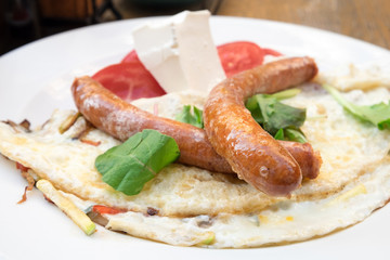 Delicious protein breakfast - grilled pork sausages served with scrambled eggs' omelette, vegetables and white feta cheese