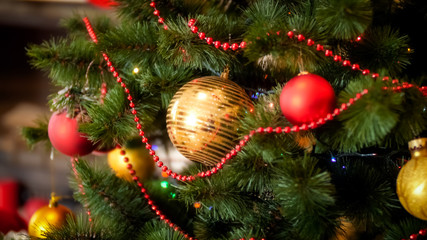 Closeup image of red and golden baubles, beads and garlands hanging on Christmas tree