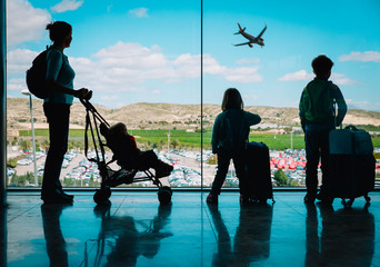 mother with kids and luggage looking at planes in airport