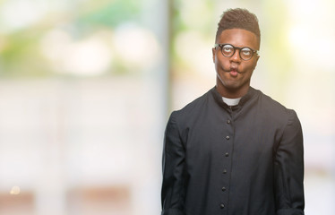 Young african american priest man over isolated background making fish face with lips, crazy and comical gesture. Funny expression.