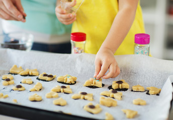 family, cooking and baking concept - mother and little daughter with sprinkles decorating cookies on tray at home kitchen